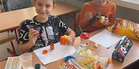 Powiększ grafikę: Dwóch chłopców siedzi w ławce i maluje farbami flispy, które kształtem przypominają dynie." Dwóch chłopców siedzi w ławce i maluje farbami flispy, które kształtem przypominają dynie.