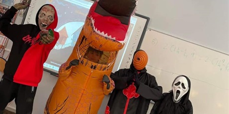 Powiększ grafikę: Troje uczniów stoi przed tablicą w klasie. Są przebrani w stroje halloweenowe.