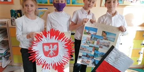 Powiększ grafikę: Dwóch chłopców trzyma plakat o Polsce. Dwie dziewczynki mają wielki emblemat z godłem Polski.
