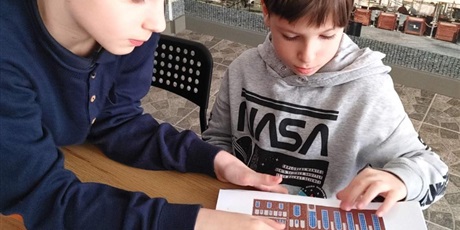 Powiększ grafikę: Dwóch chłopców oglądających książkę napisana alfabetem Braille”a. Z tylu tapeta na ścianie z kamieniczkami Gdańska