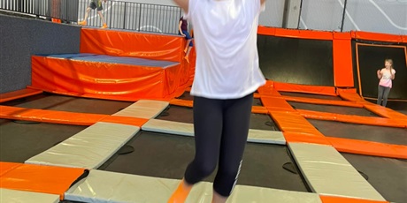 Powiększ grafikę: Dziewczynka w białej koszulce, skacząc do góry, odbijając się od trampoliny