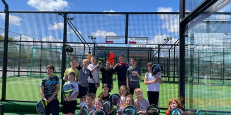 Powiększ grafikę: Na tle bolisk do tenisa, grupa uśmiechniętych dzieci pozująca do zdjęcia  z paletkami w ręku.