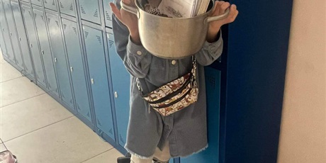 Powiększ grafikę: Dziewczynka stoi przy szafkach szkolnych, w ręku trzyma garnek z książkami.
