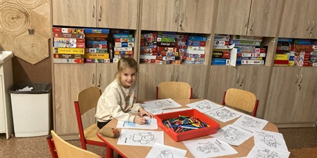 Powiększ grafikę: Dziewczynka koloruje kolorowanki w sali świetlicowej na tle gier planszowych