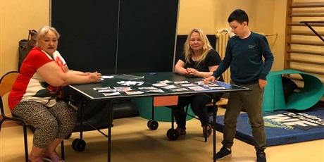 Powiększ grafikę: Dwie nauczycielki siedzą przy stole do ping-ponga. Podszedł do nich uczeń, który układa kartki.
