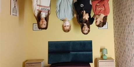 Powiększ grafikę: Na dole na zdjęciu łóżko i dwie szafeczki, na suficie cztery dziewczynki stojące głowami w dół