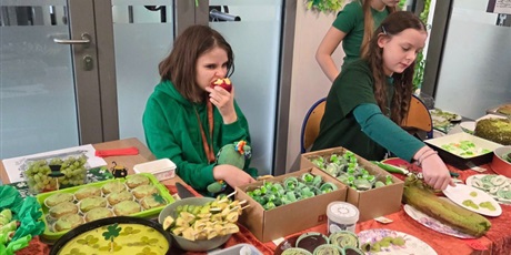 Powiększ grafikę: Trzy dziewczynki, ubrane na zielono siedzą przy stole z zielonymi przekąskami