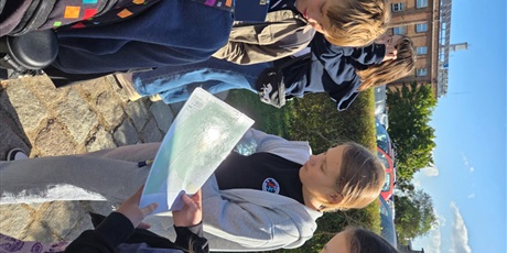 Powiększ grafikę: Dziewczynka patrzy na mapę, obok inni uczniowie przygotowują się do gry.