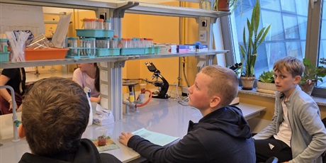 Powiększ grafikę: Troje uczniów siedzi przy stanowiskach w laboratorium chemicznym