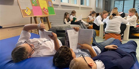 Powiększ grafikę: Chłopcy leżą i czytają wspólnie książki, a w tle widać pozostałe dzieci, które znajdują się w Strefie Czytania.