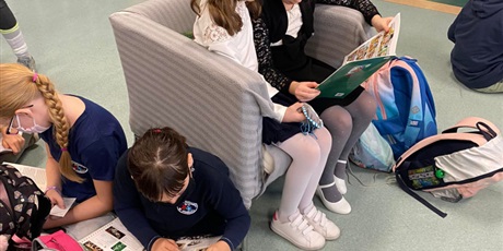 Powiększ grafikę: Cztery dziewczynki czytają książki. Dwie z nich siedzą na fotelu, a pozostałe dwie na ziemi. 