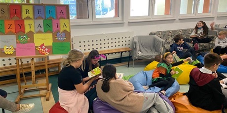 Powiększ grafikę: Uczniowie siedzą na pufach i kanapie i czytają książki. W te widać napis: Strefa Czytania. 