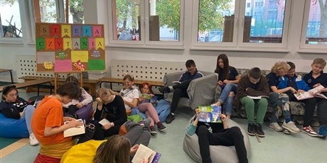 Powiększ grafikę: Uczniowie siedzą na pufach i kanapie i czytają książki. W te widać napis: Strefa Czytania. 