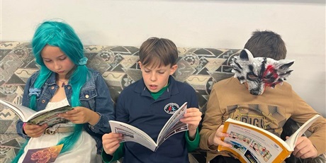 Powiększ grafikę: Trójka dzieci na kanapie czyta książkę. Dziewczynka ma perukę z niebieskimi włosami, a jeden z chłopców przebrany jest za wilka. 