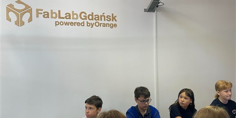 Powiększ grafikę: Grupa uczniów siedzących przy komputerach. Na ścianie napis FabLabGdansk powered by Orange