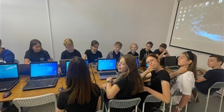 Powiększ grafikę: Grupa uczniów siedząca przy komputerze. Dwie dziewczynki uśmiechają się do zdjęcia