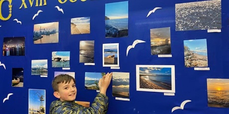 Powiększ grafikę: Chłopiec wskazuje na swoją pracę fotograficzną, która znajduje się wśród innych  zdjęć. 