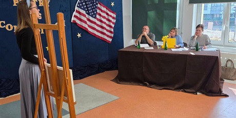 Powiększ grafikę: Dziewczynka, obok niej sztaluga ze zdjęciem stoi przed jurorami i prezentuje wiersz