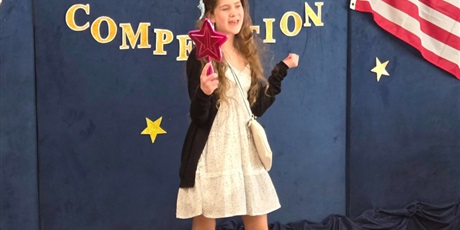 Powiększ grafikę: Dziewczynka w białej sukience z rekwizytami recytuje wiersz, na tle dekoracji