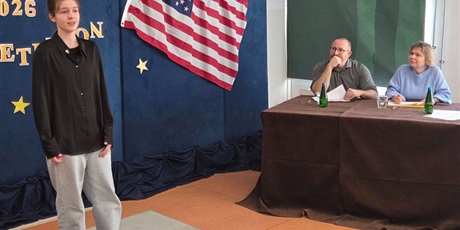 Powiększ grafikę: Dziewczynka ubrana w czarną koszulę i jasne spodnie recytuje wiersz, po lewej jurorzy