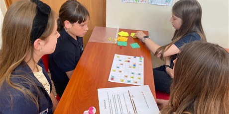 Powiększ grafikę: Cztery dziewczynki grają w grę planszową utworzoną przez swoje koleżanki z klasy. Widać planszę do gry i kolorowe karty.