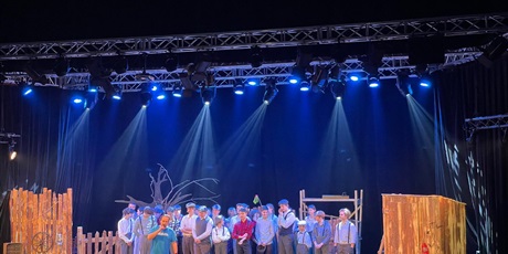 Powiększ grafikę: Aktorzy stojący na scenie w świetle reflektorów.