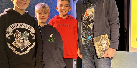 Powiększ grafikę: Trzech chłopców stoi obok pisarza Jana Bliźniaka. Autor trzyma powieść " Śrubek i tajemnice Maszynerii"